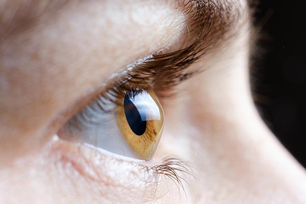 The image shows a close-up view of a human eye with visible iris details against a blurred background.