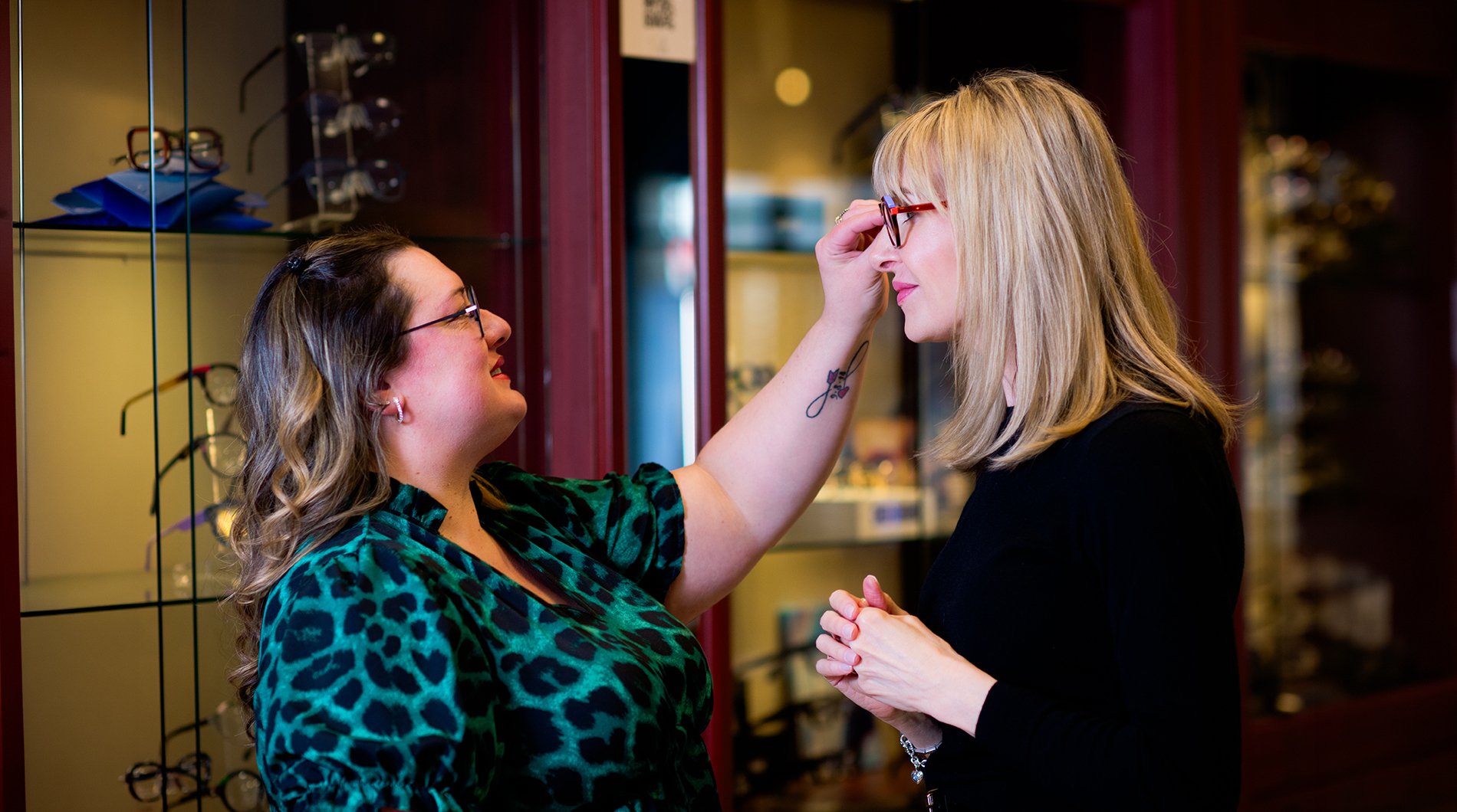 Woman applying makeup on another woman with glasses in the background.