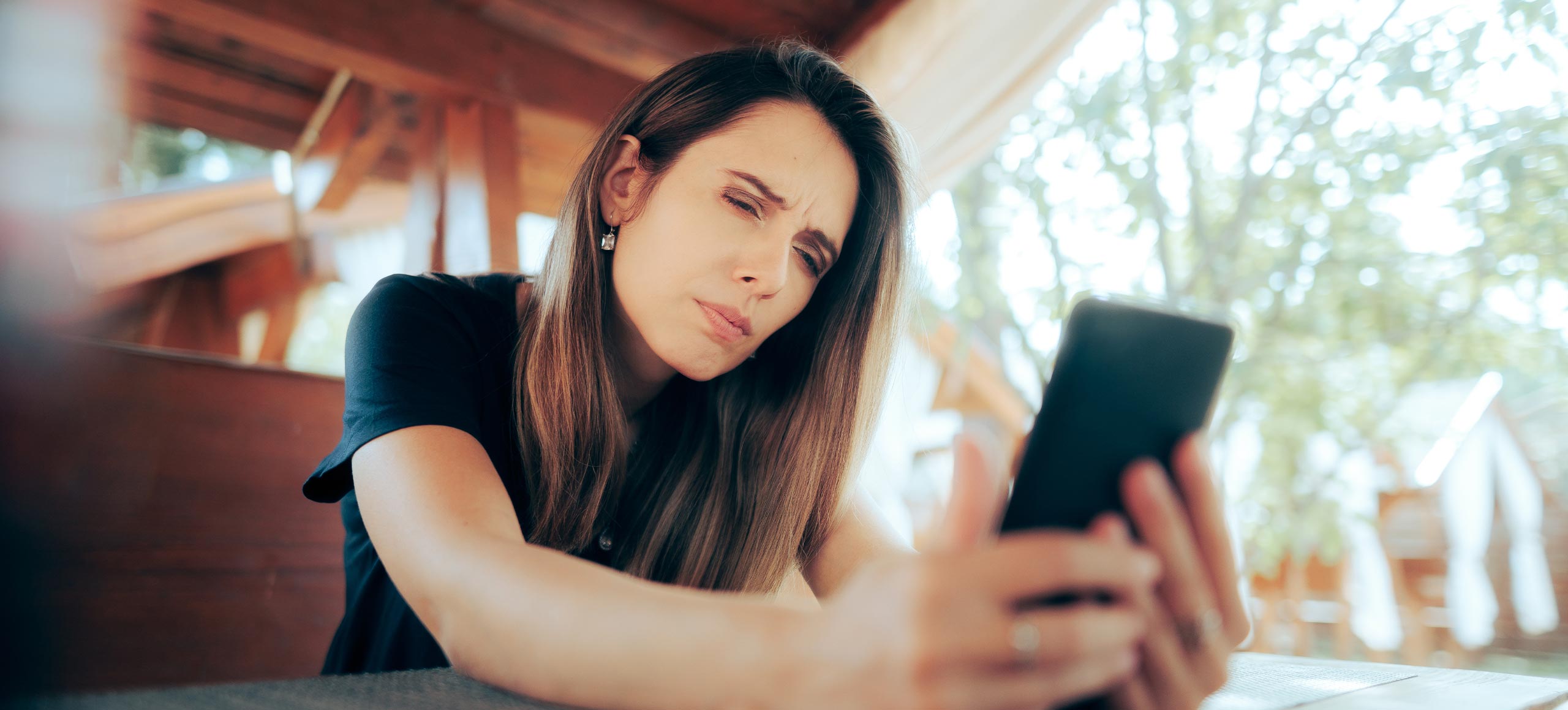 A woman sitting at a table, looking at her phone with a neutral expression.