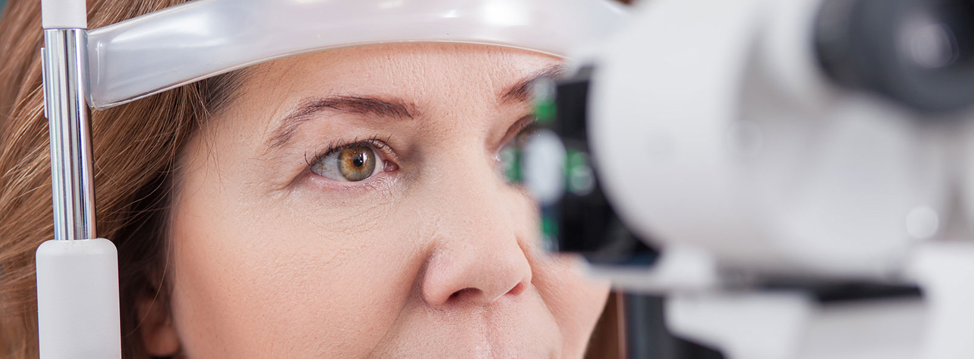 A woman with glasses looking into a medical device, possibly an eye exam machine, with a focused expression.