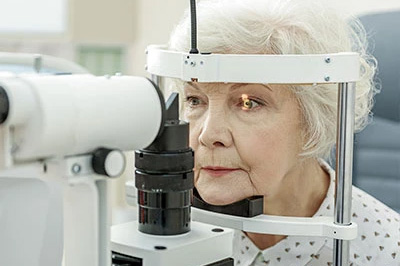 Woman sitting at an eye test machine with her eyes open wide.