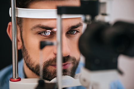 The image shows a man with blue eyes looking into an eye machine, likely at an optometrist s office, with a focus on his face and the equipment he is using.