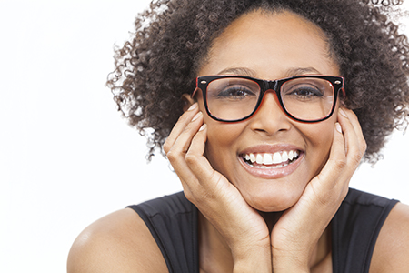 The image features a woman with curly hair smiling at the camera, wearing glasses and a black top, with her hands on her cheeks.