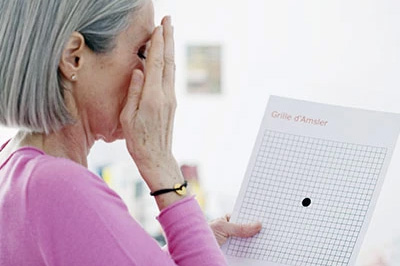 The image shows a person holding a piece of paper with a grid pattern, looking at it with a hand covering their eyes, presumably reading or examining the content.